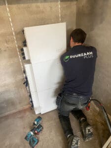 Een installateur van Duurzaam Plus is een thuisbatterij aan het installeren in een schuur.